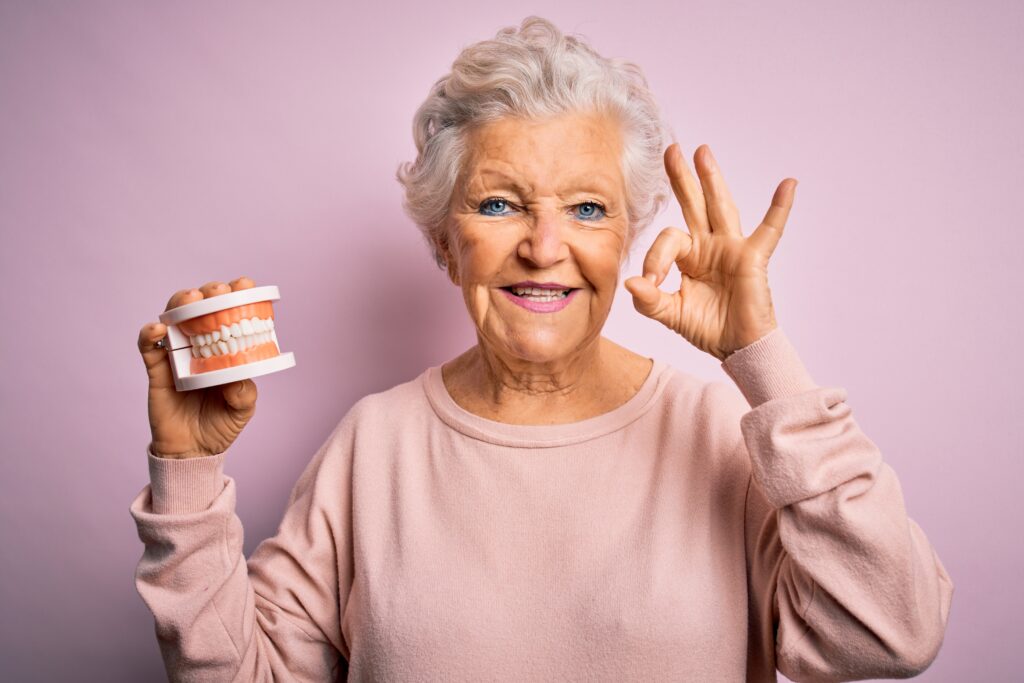ältere Dame, fröhlich, hält Zahnmodell in die Kamera, Dental Longevity